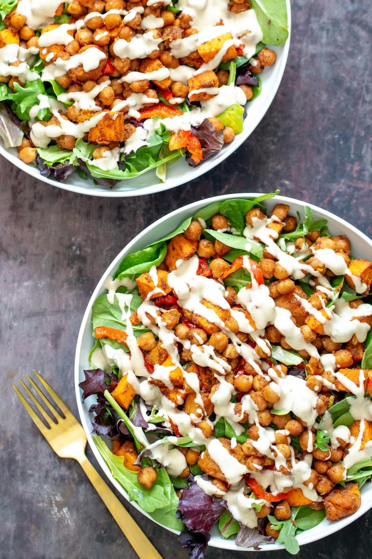 sweet potato salad two bowl with leafy greens topped with roasted chickpeas and cubed sweet potato
