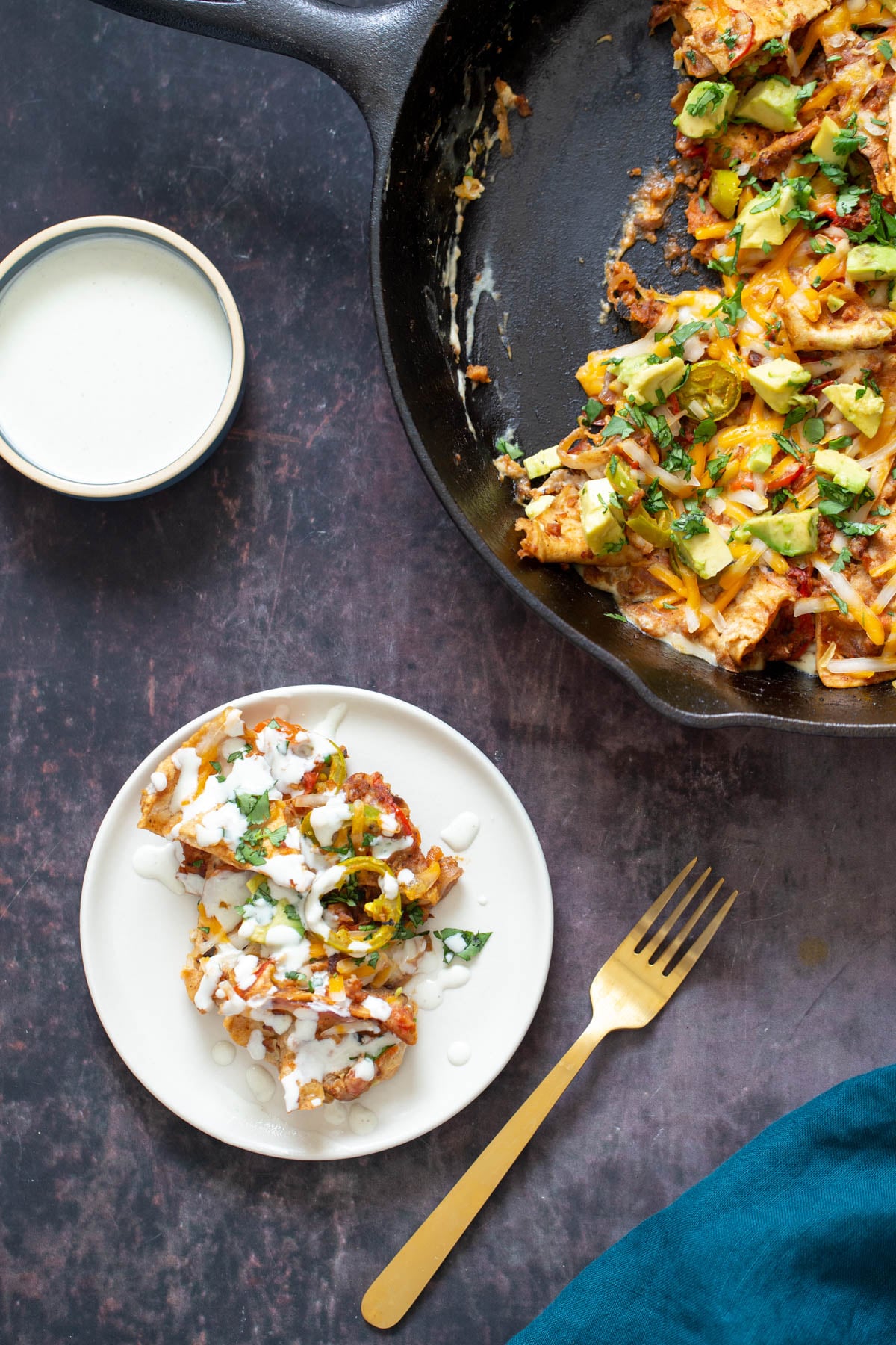 a serving of vegan jalapeno popper skillet served on a small white plate next to a skillet and a dish with cashew cream