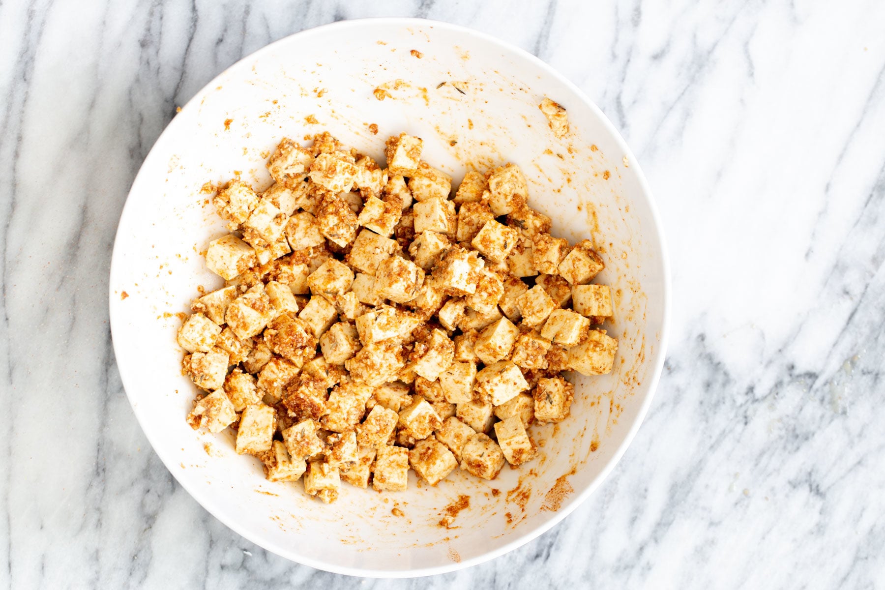 marinated cubed tofu being mixed with crunch topping