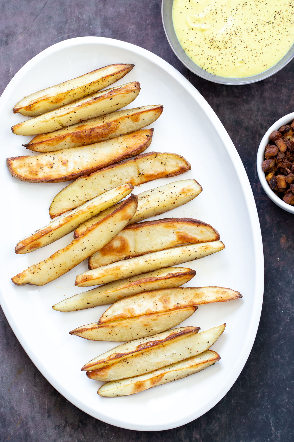 loaded potato wedges a platter of crispy vegan baked potato wedges next to a small bowl of queso and tofu bacon
