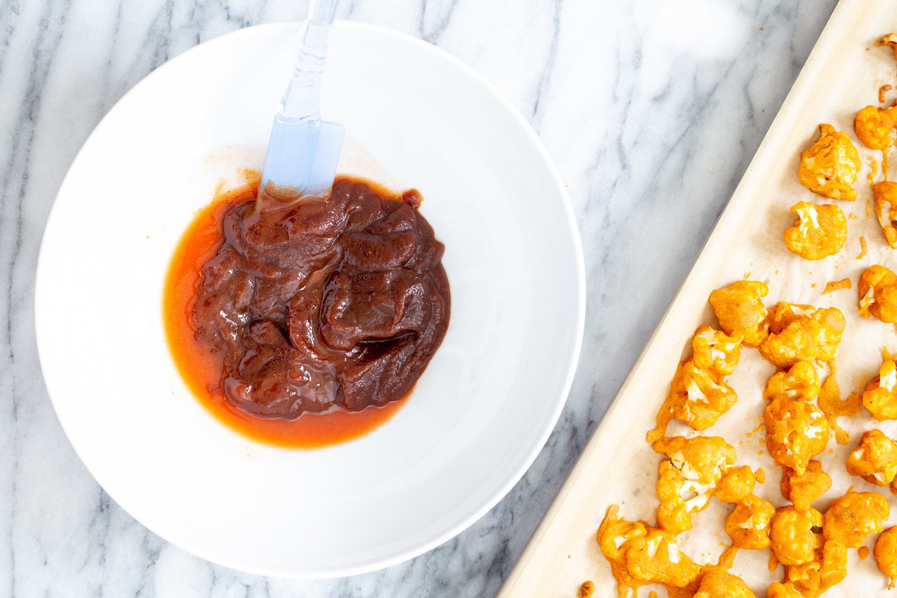 cauliflower wings hot sauce and bbq sauce being mixed in a small dish