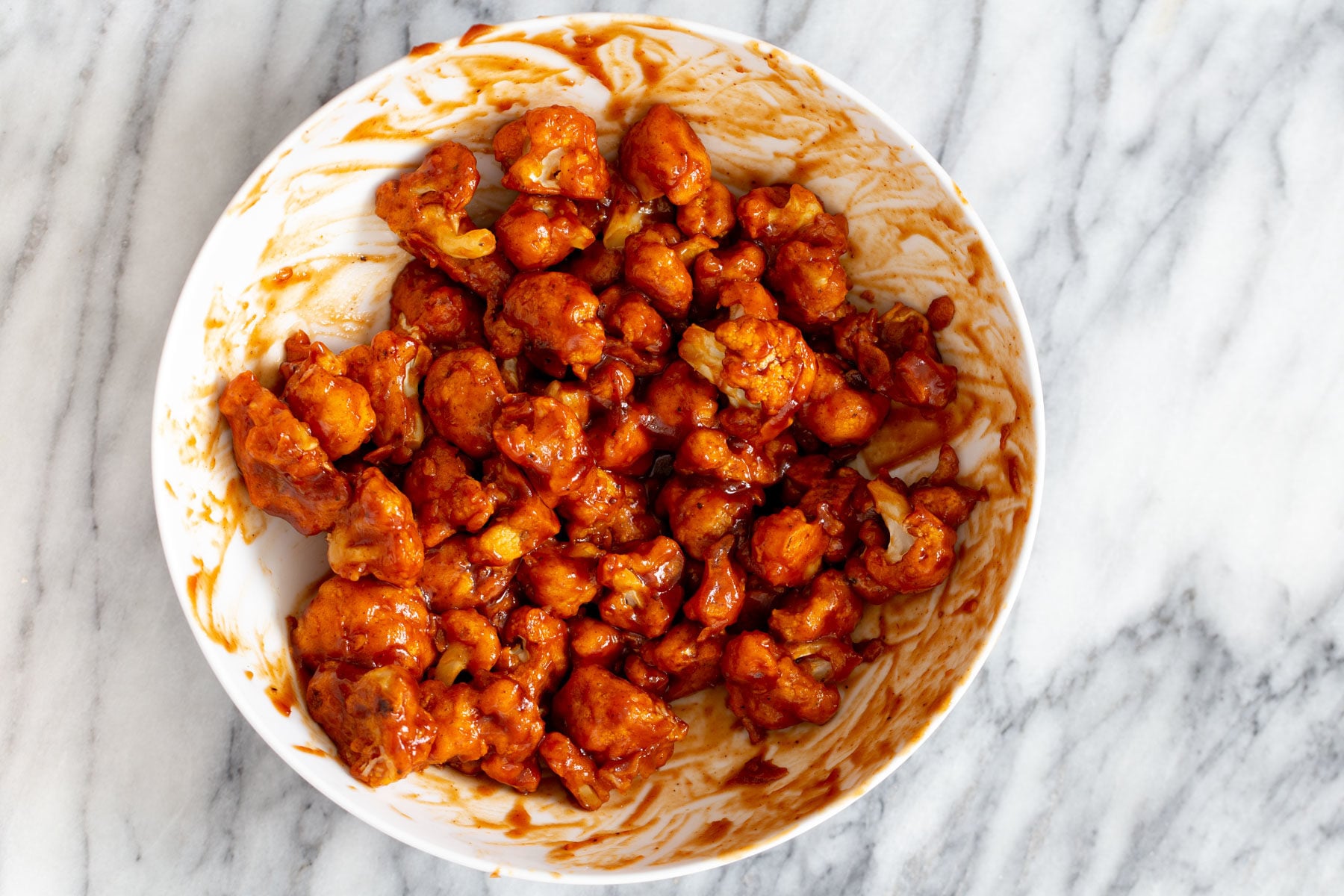 cauliflower wings baked cauliflower wings being tossed in a small bowl with spicy bbq sauce