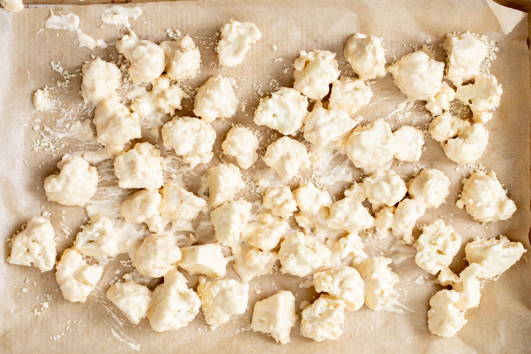 battered cauliflower florets on a lined baking sheet