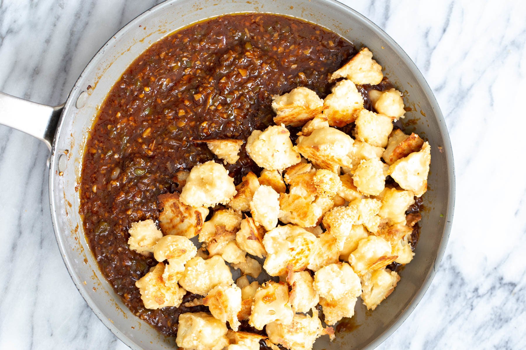 cauliflower manchurian breaded baked cauliflower florets being added to Manchurian sauce in a pan