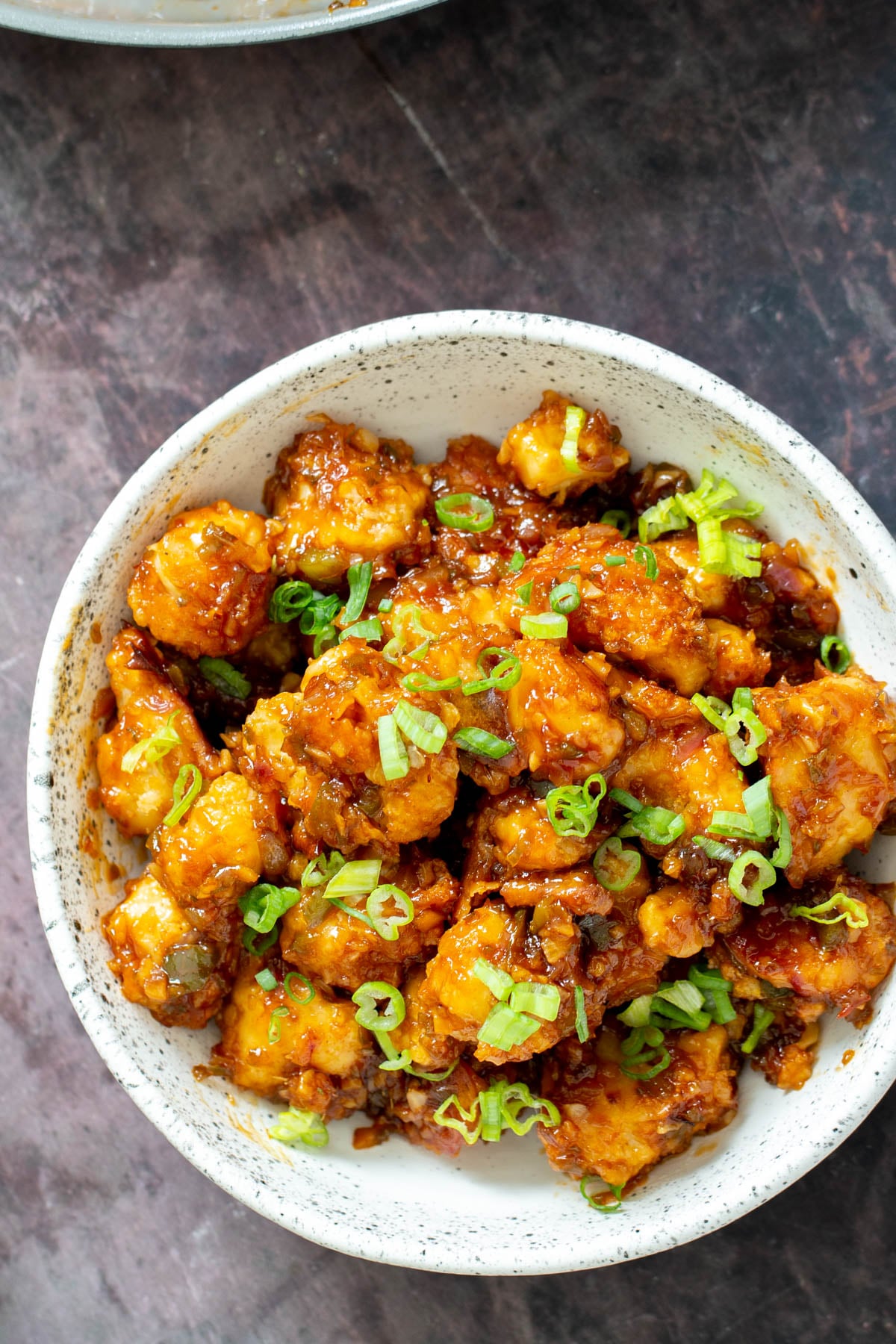 Cauliflower Manchurian a white bowl with vegan gobi Manchurian topped with thinly sliced scallions