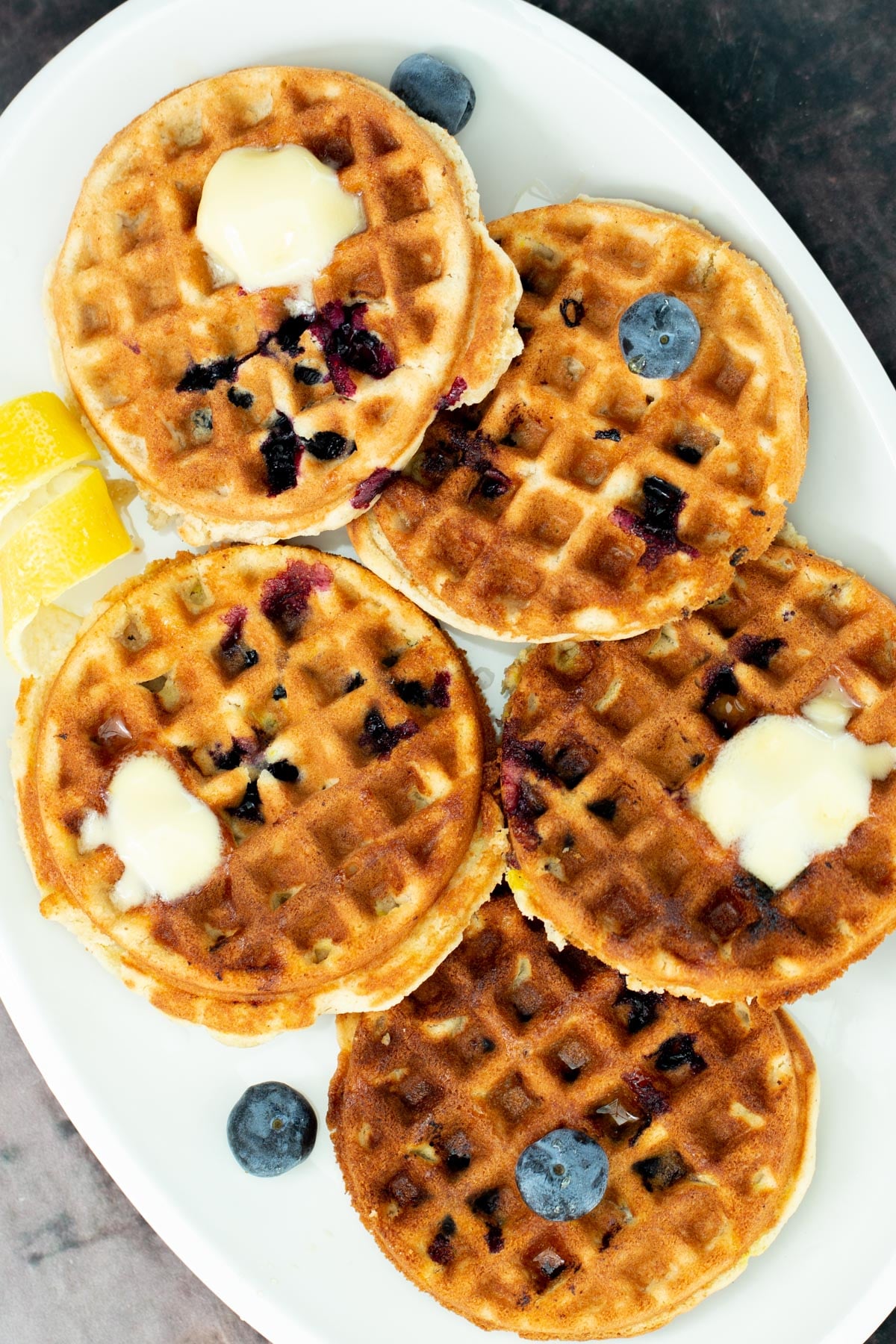 a plate of vegan glutenfree lemon blueberry waffles topped with dollops of butter and fresh blueberries