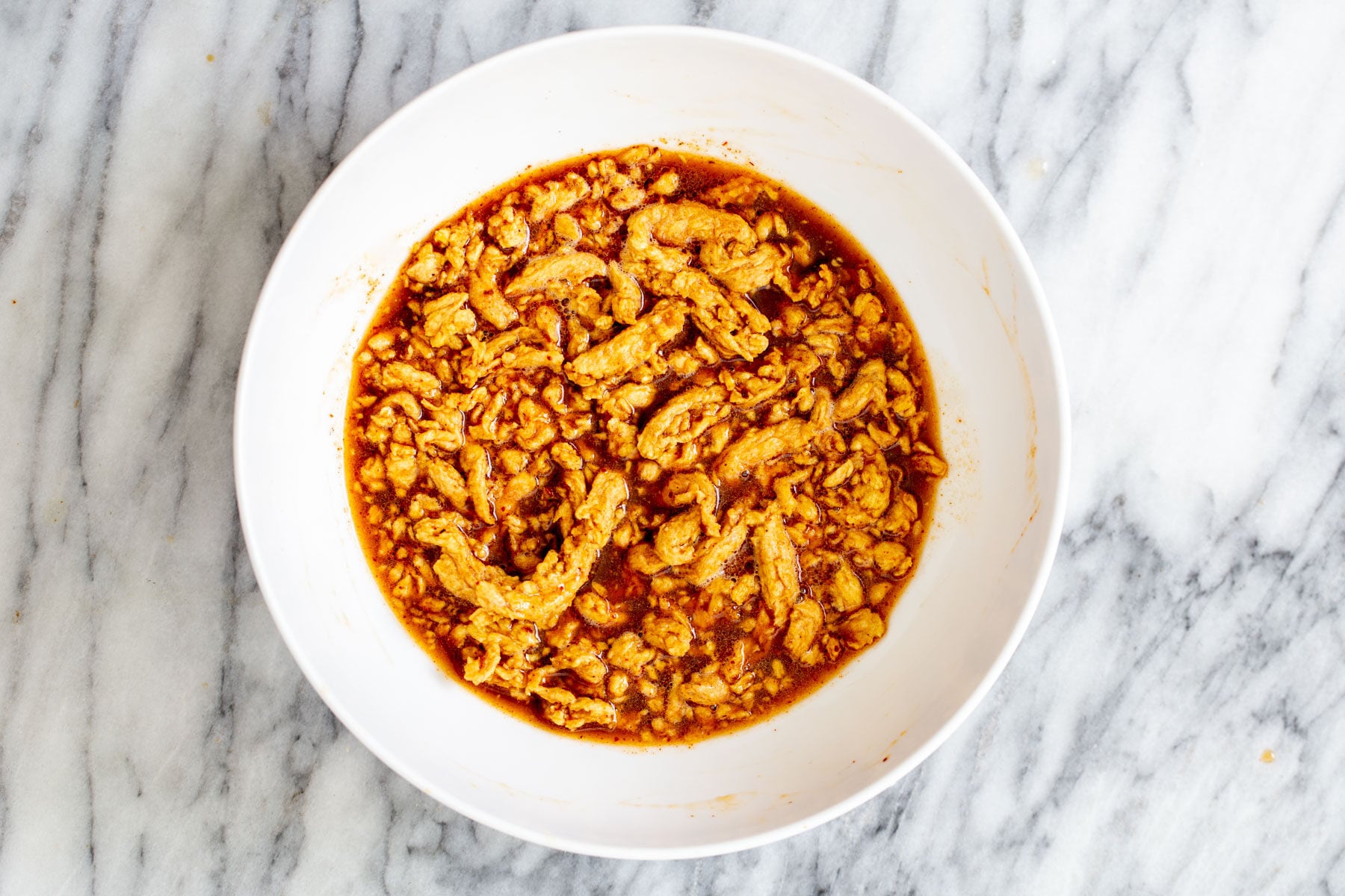 vegan crunchwrap soy curls being marinated in korean bbq marinade in a white bowl