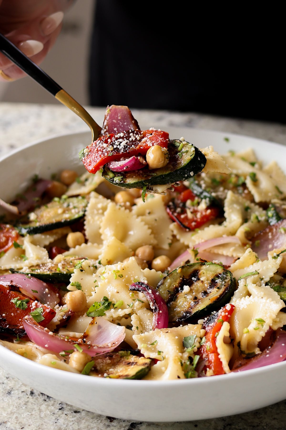 spooning a bite of summer pasta salad with grilled vegetables