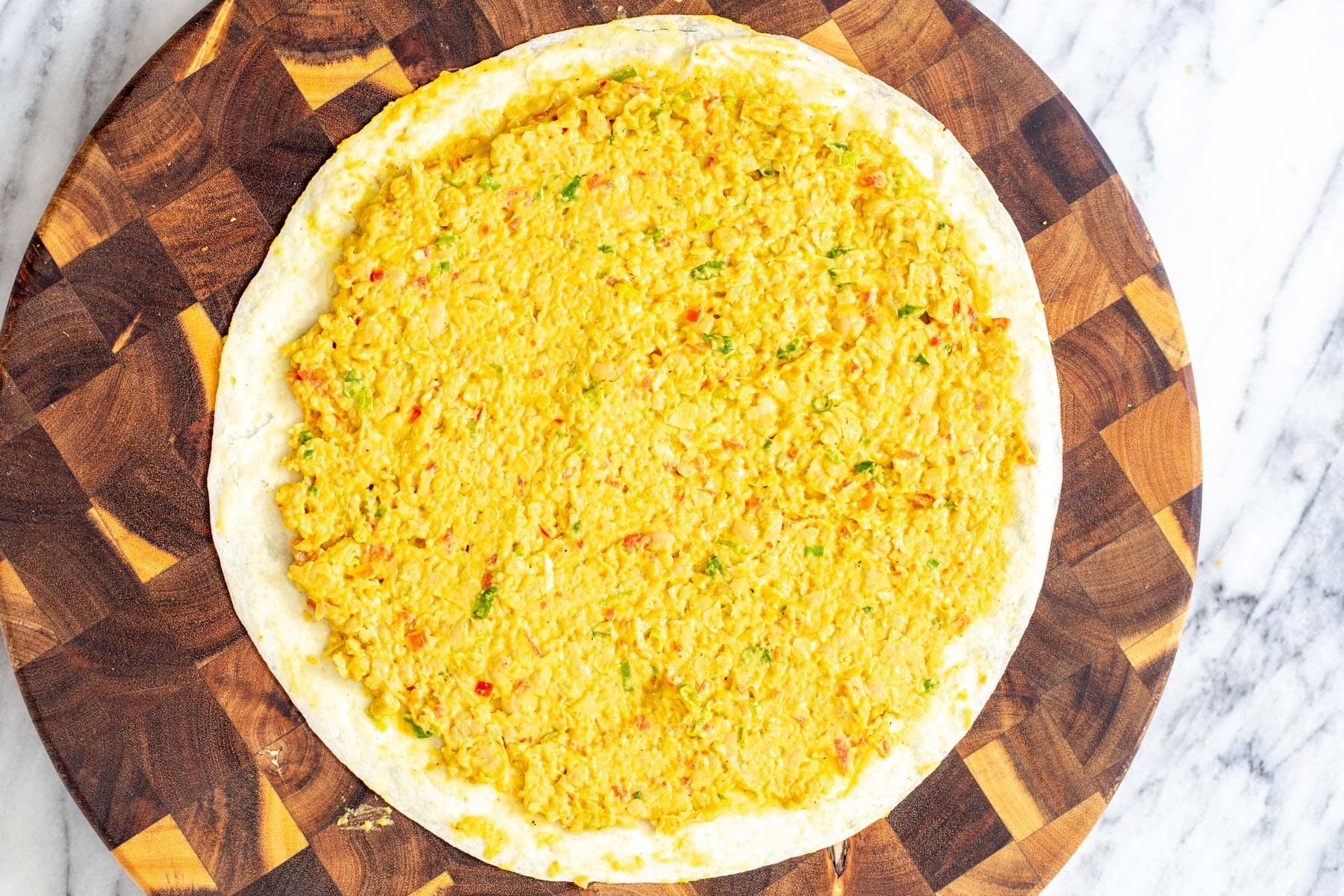 a flour tortilla being topped with vegan chickpea scramble