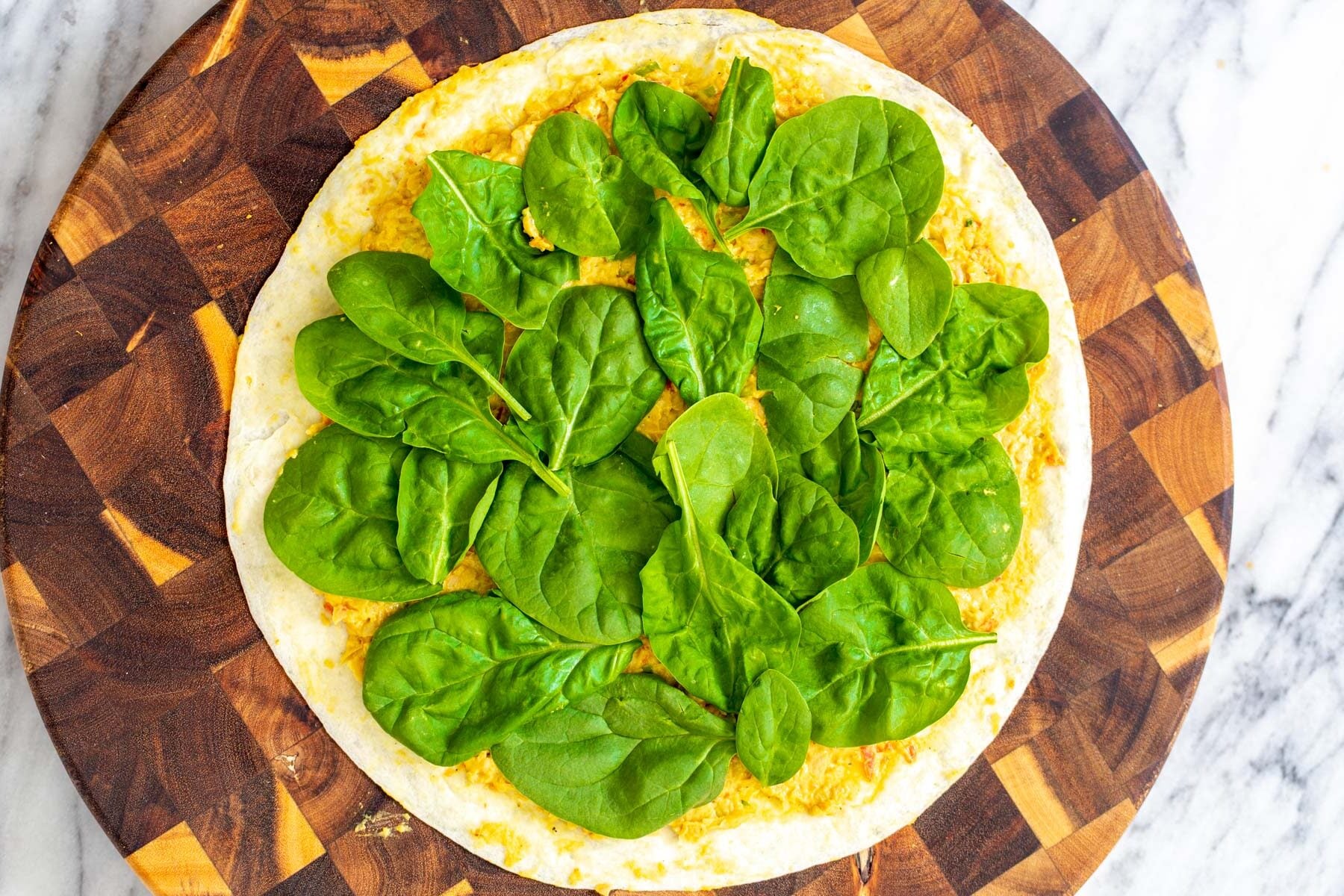 tortilla topped with chickpea scramble and fresh spinach on a wooden board