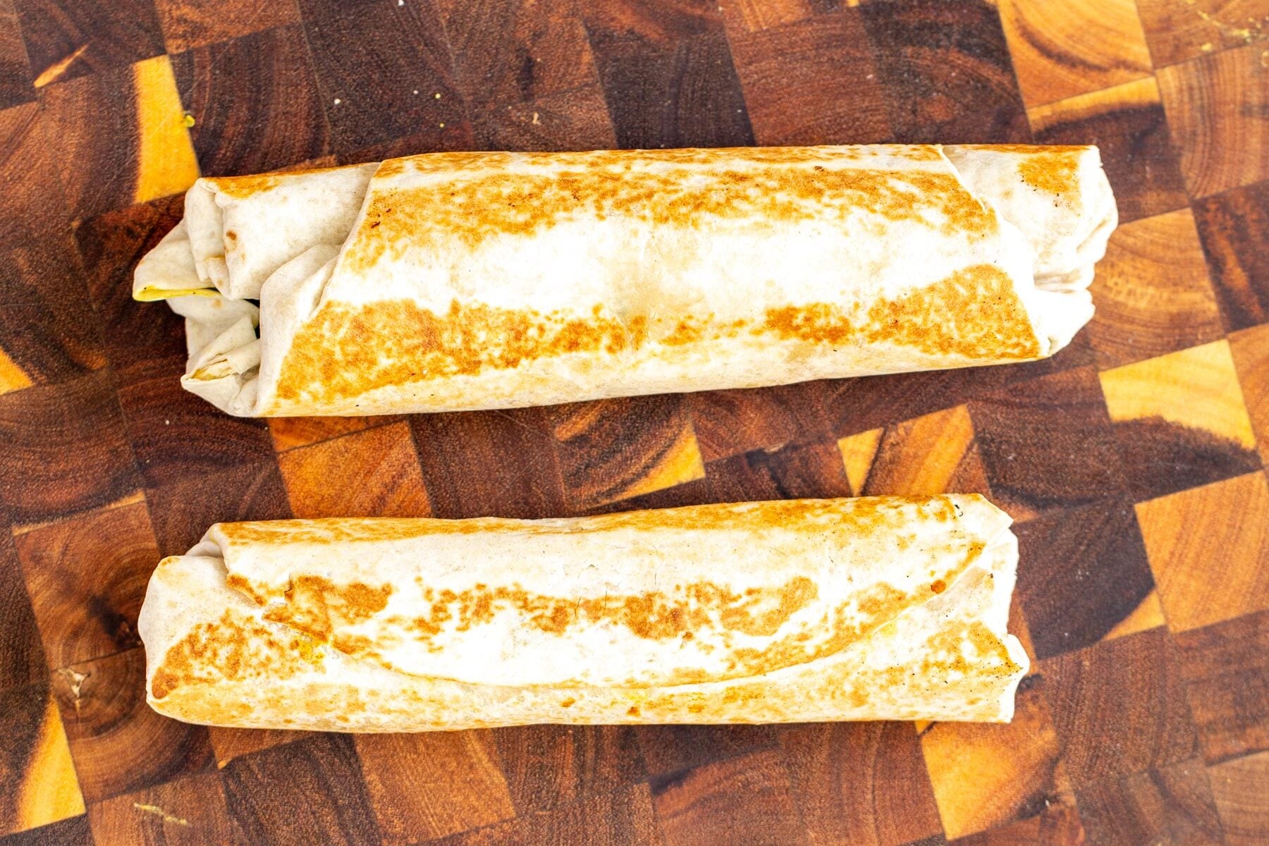 two vegan chickpea breakfast wraps rolled up on a wooden board 