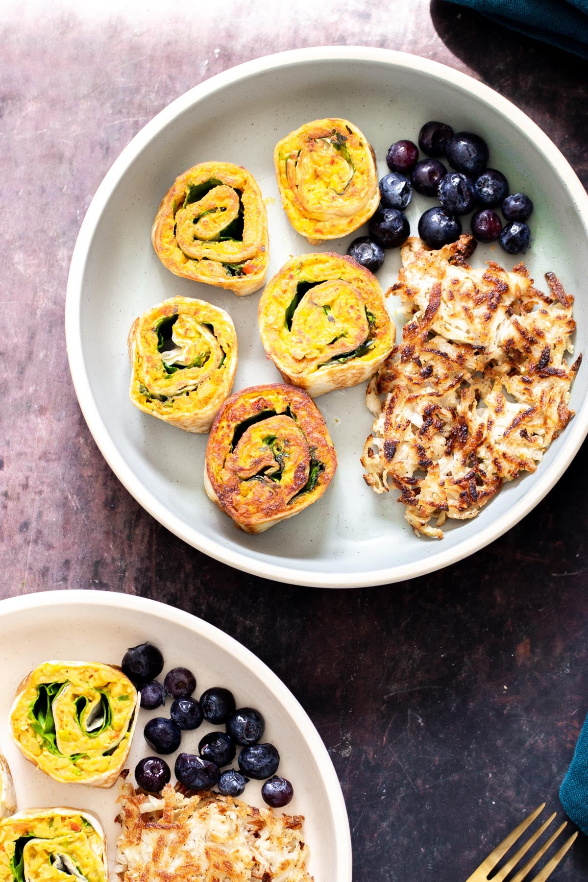 two plates with sliced vegan chickpea scramble wraps served with hashbrowns and berries