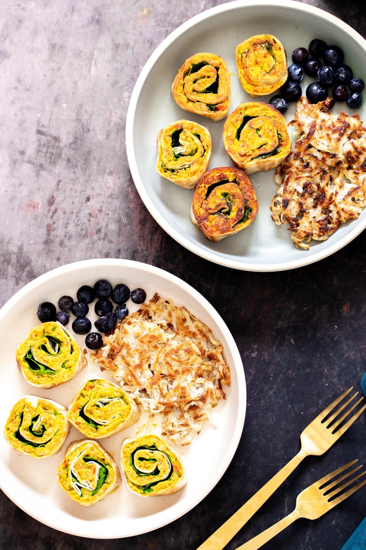two plates with vegan chickpea breakfast scramble pinwheels served with berries and hashbrowns