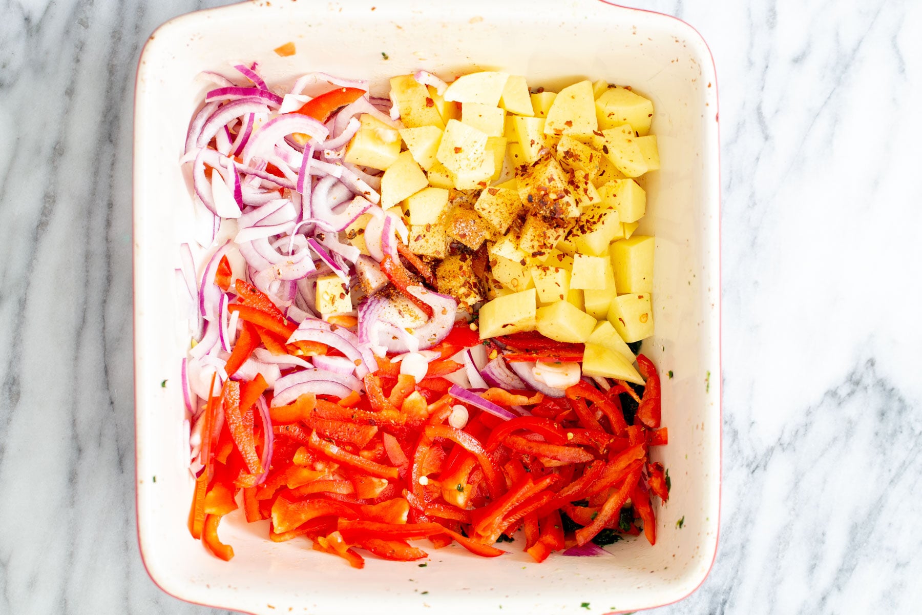 sliced onion and bell pepper and cubed potatoes in a white casserole dish