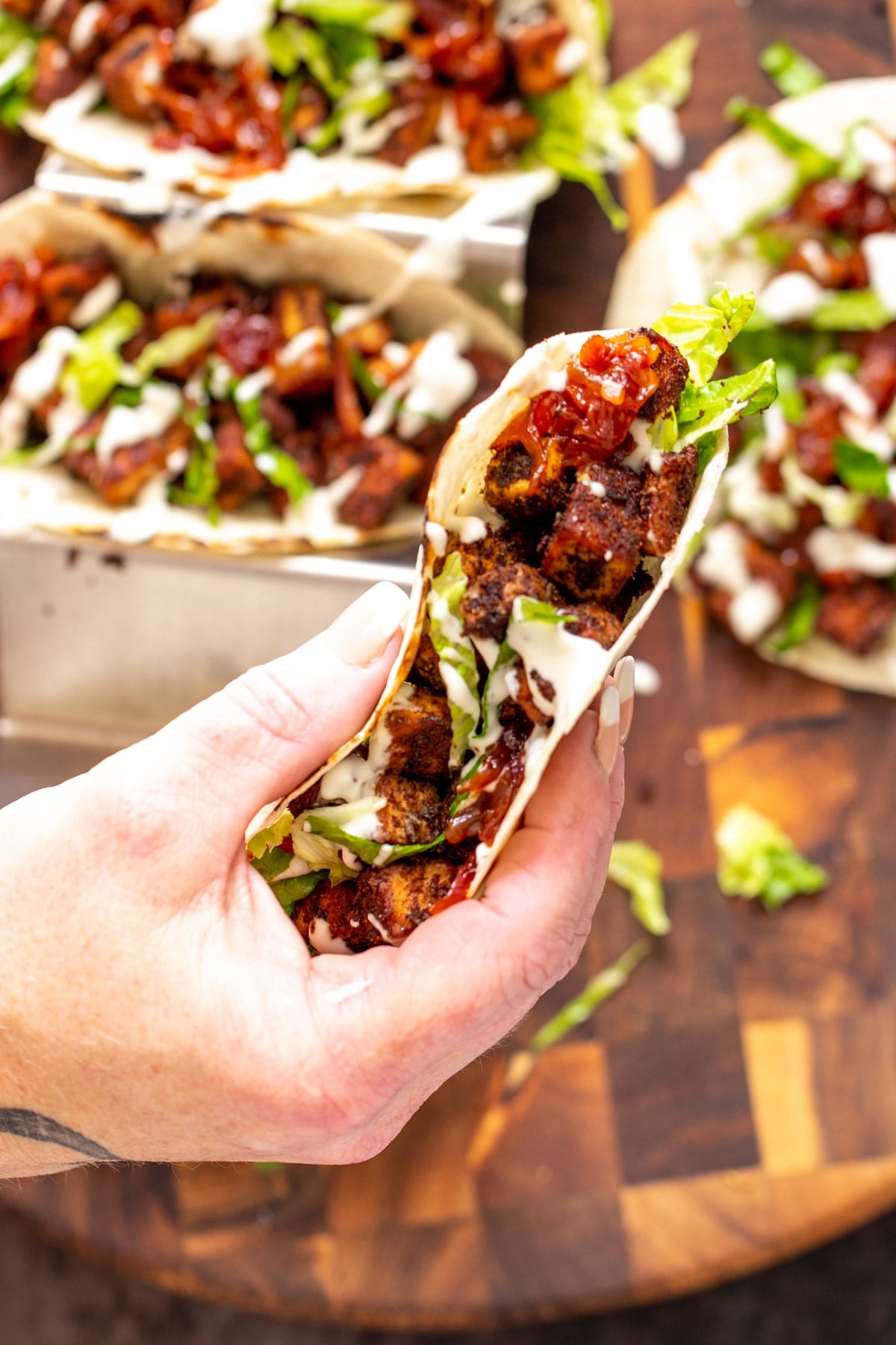 blackened tofu tacos a hand holding a vegan blackened tofu taco drizzled with sour cream and filled with caramelized onions