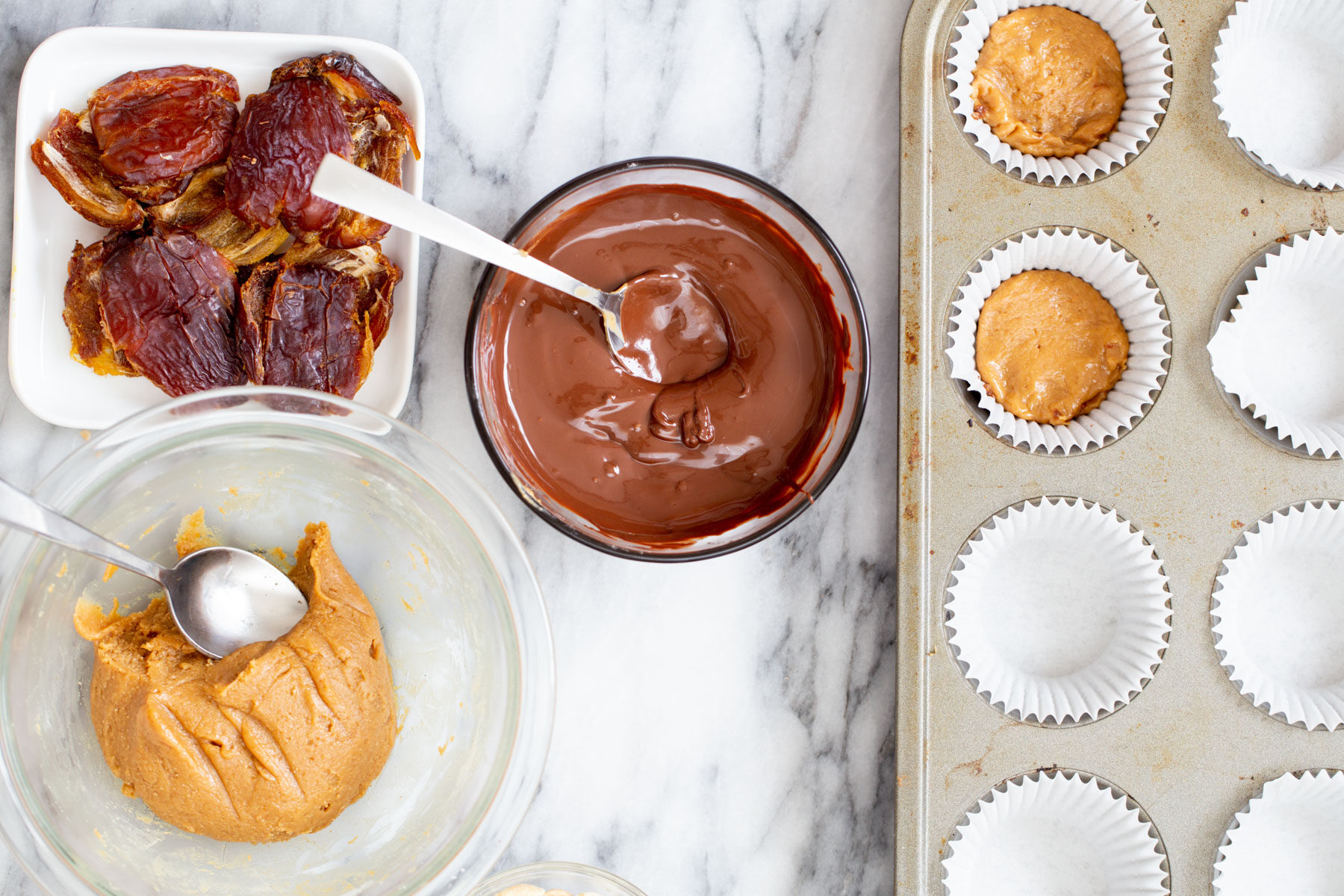 mini muffin liners being filled with melted chocolate and peanut butter to make vegan snickers cups