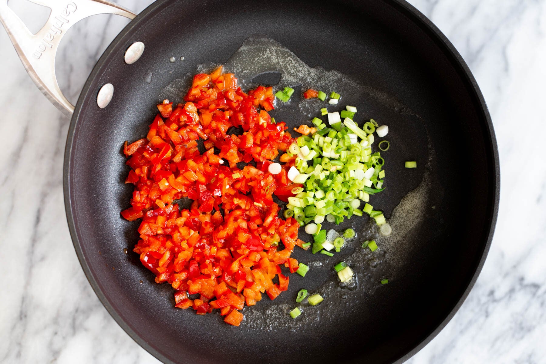 tofu scramble seasoning bell pepper and green onions in a sauteeing pan