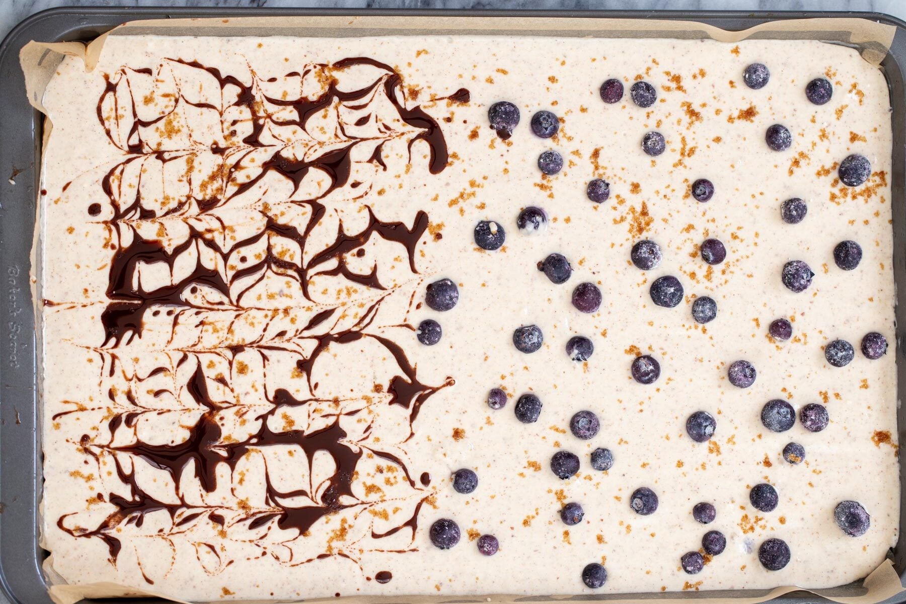 vegan sheet pan pancakes a sheet pan with pancake batter half topped with blueberries, half swirled with cinnamon syrup