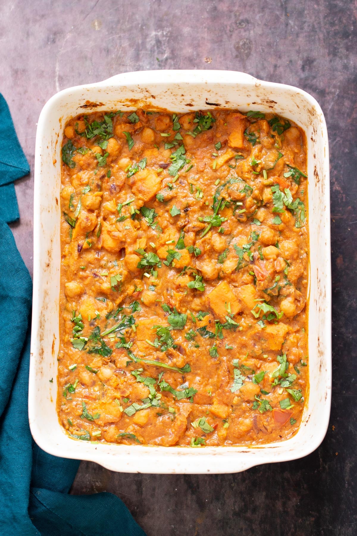 Top shot of casserole dish with chickpea sweet potato curry, blue green kitchen napkin on the side