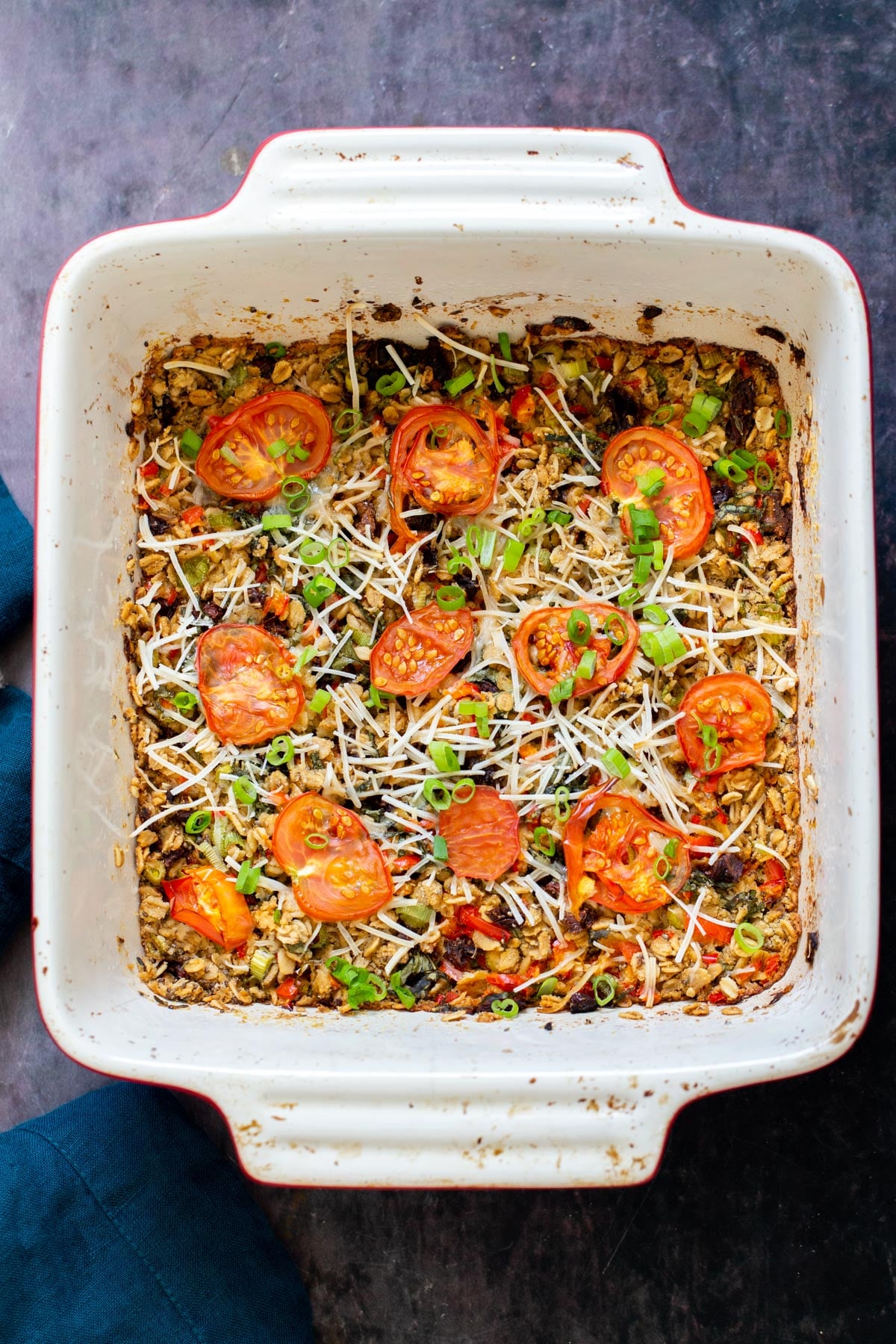 a casserole dish with savory pizza oatmeal bake topped with shredded mozarella and tomatoes