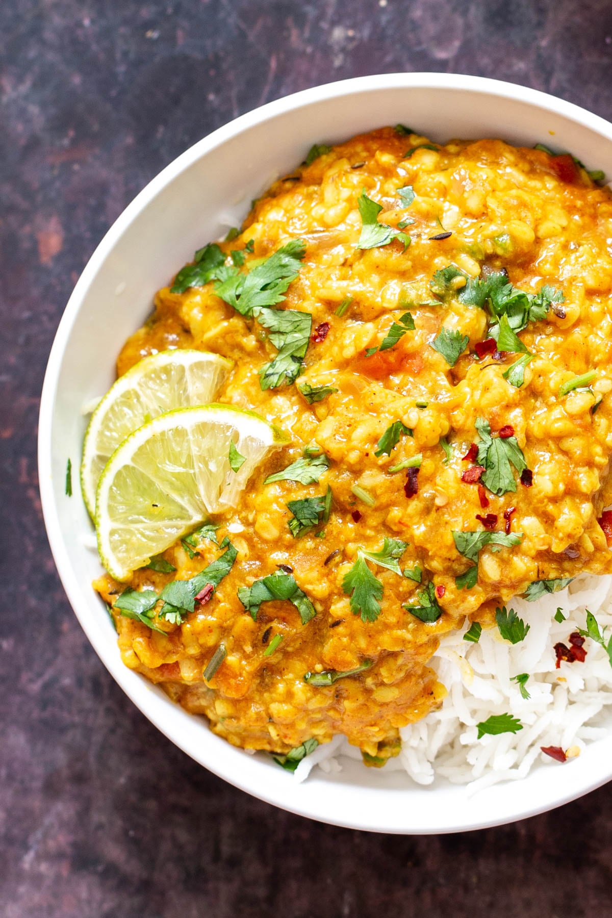 spicy urad dal served over rice with some lime slices and sprinkled with cilantro 
