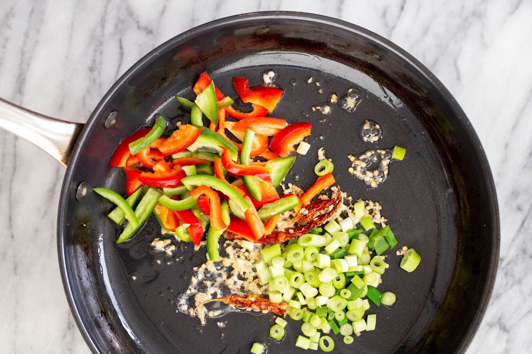 bell peppers spring onions and garlic in a frying pan