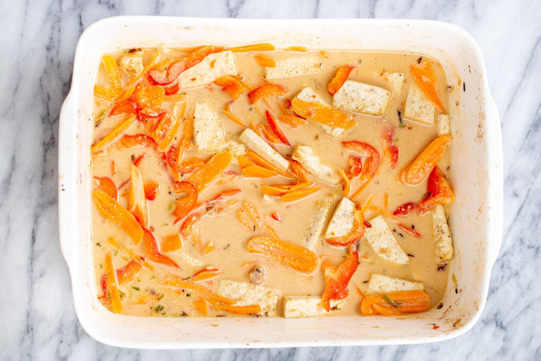 coconut milk being added to a casserole dish with veggies and tofu