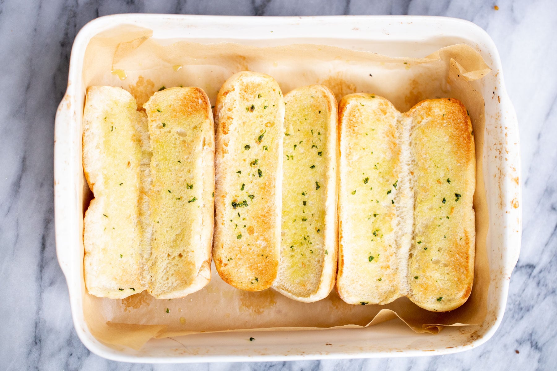 sliced open Italian baguette buns in a white casserole dish