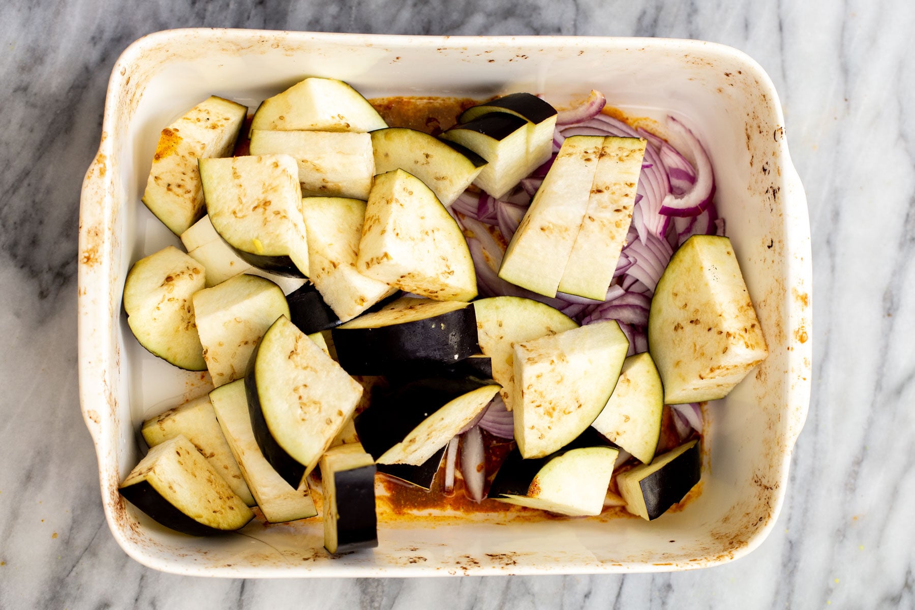 eggplants and onion slices in a white casserole dish