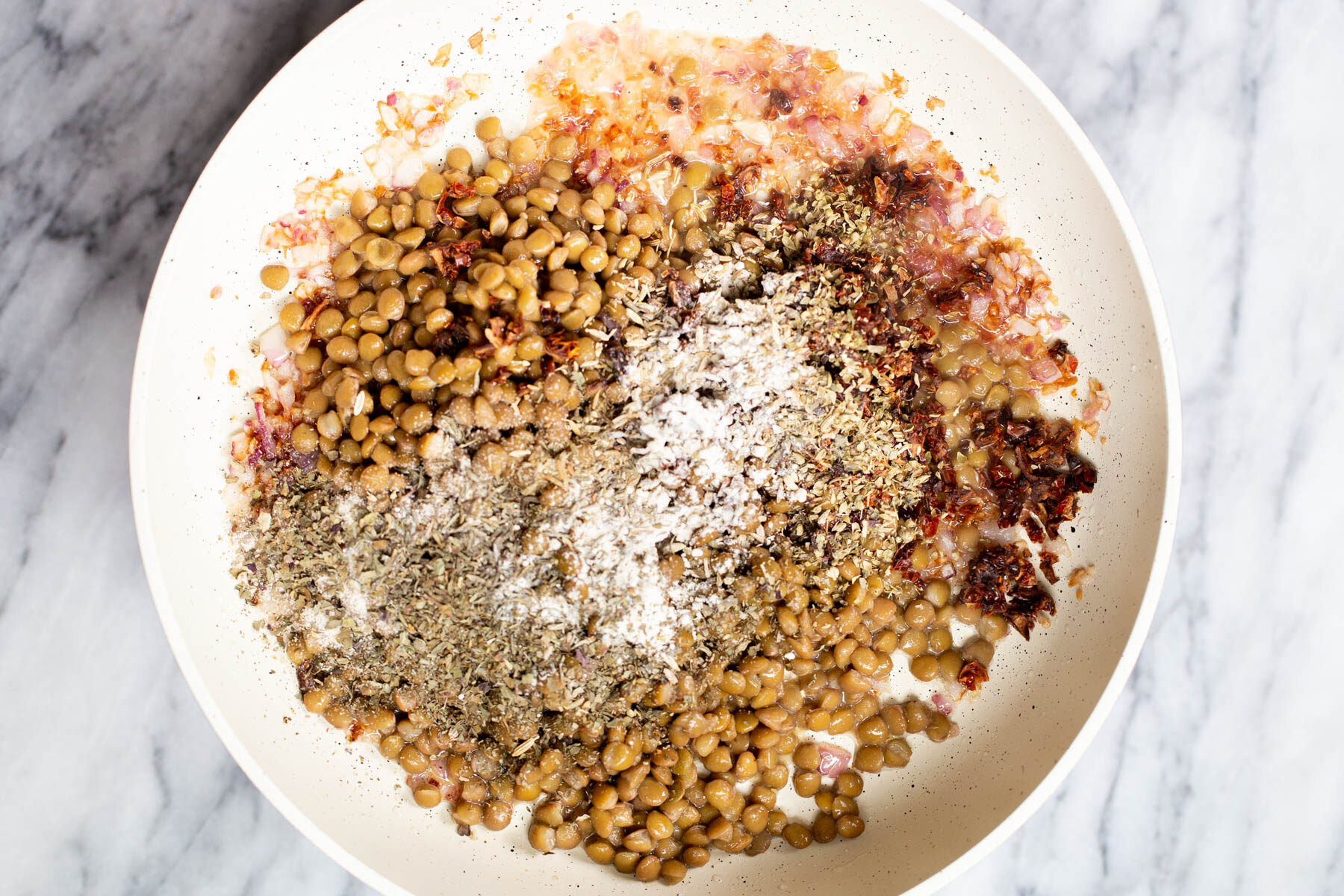 spices being sprinkled over brown lentils in a sauteeing pan