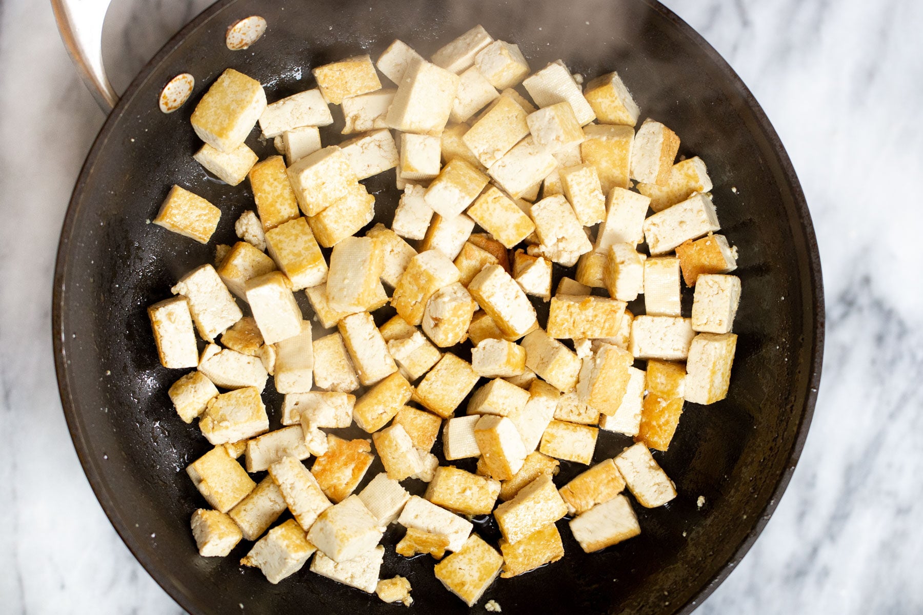 tofu cubes being fried in a black skillet