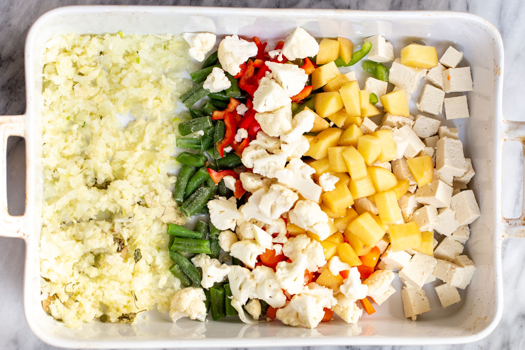 Navratan Korma tofu cubes, veggies and minced ginger and garlic in a white casserole dish
