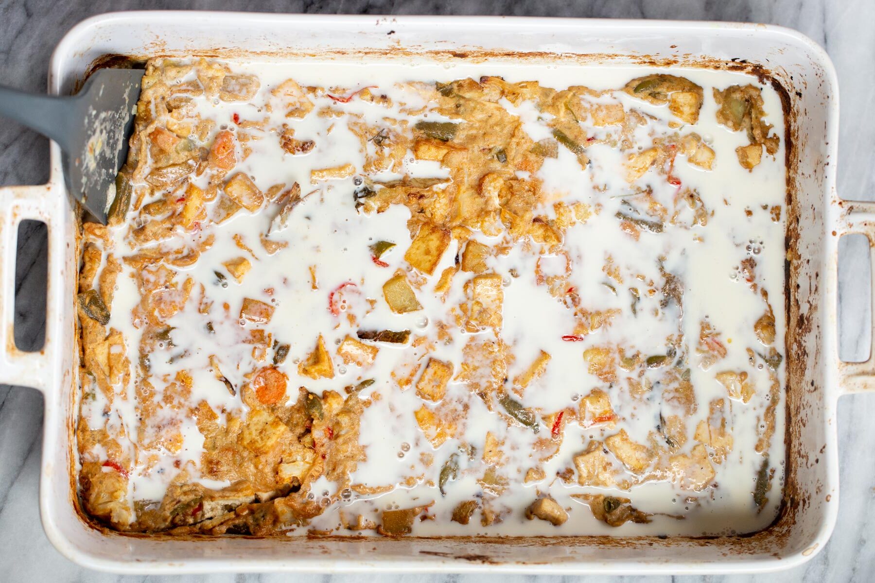 Navratan Korma milk being added to tofu and veggies in a white casserole dish