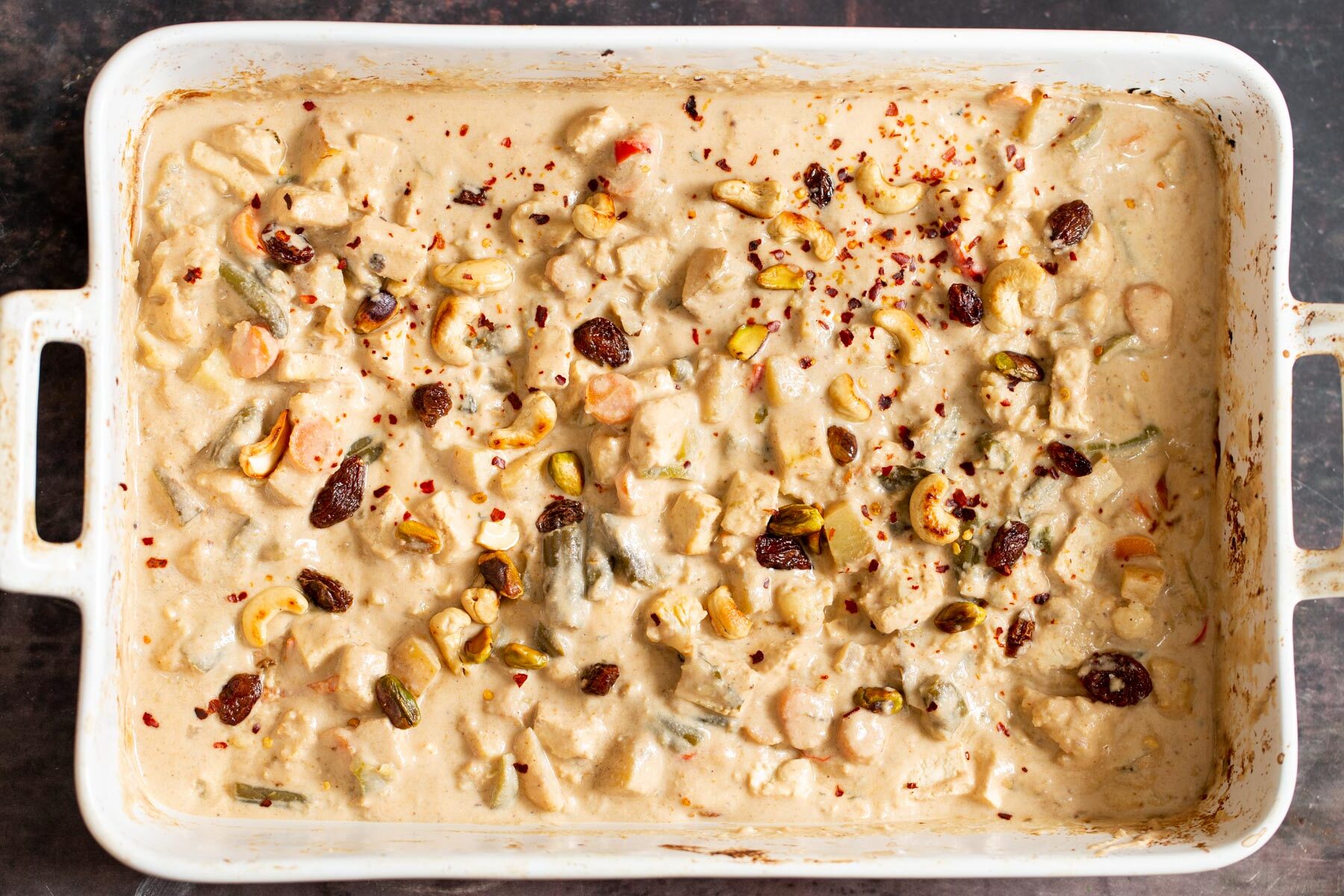 creamy Indian Navratan Korma curry in a white casserole dish sprinkled with nuts and chili flakes