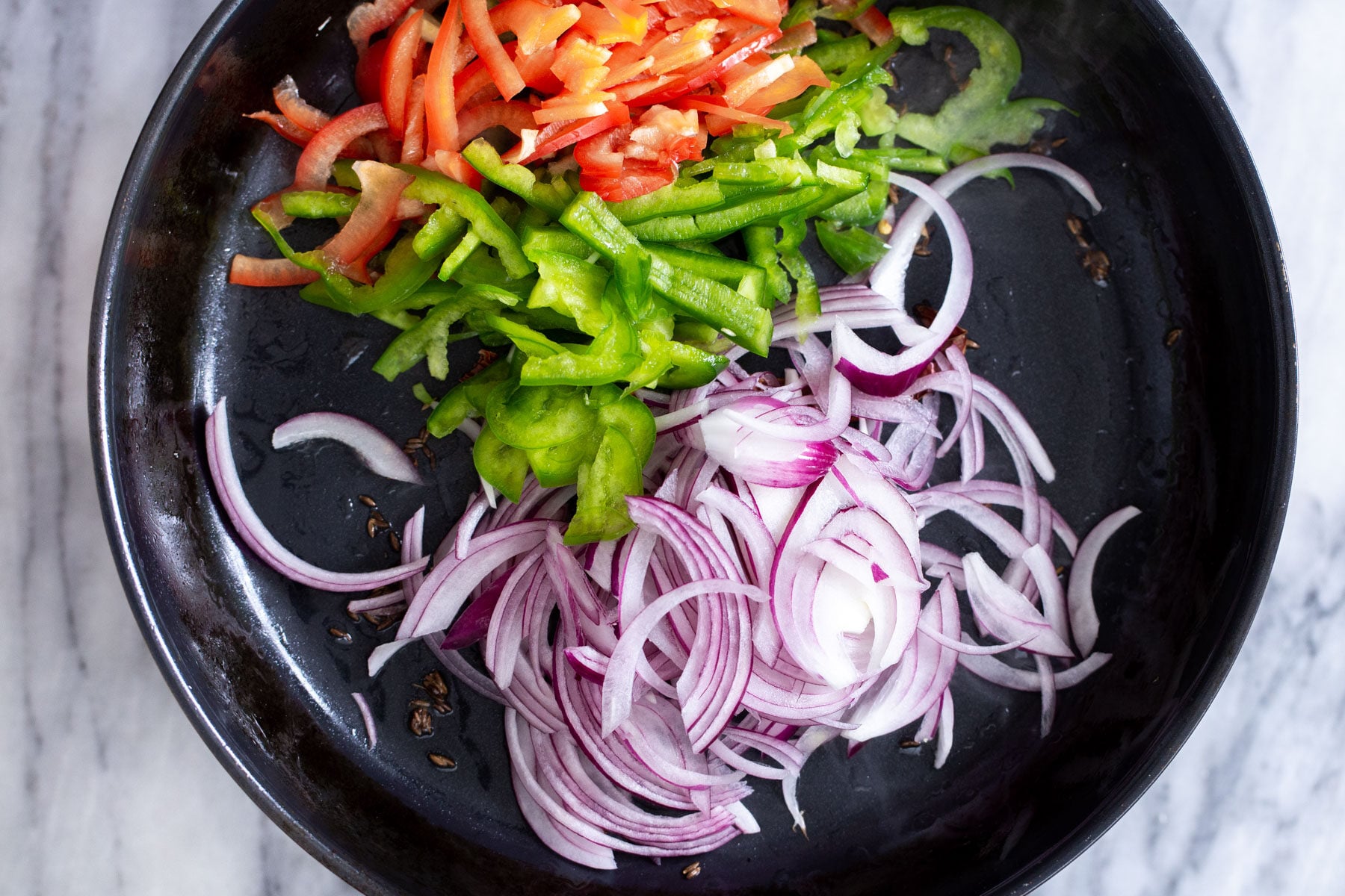 sliced bell peppers and onions being added to skillet