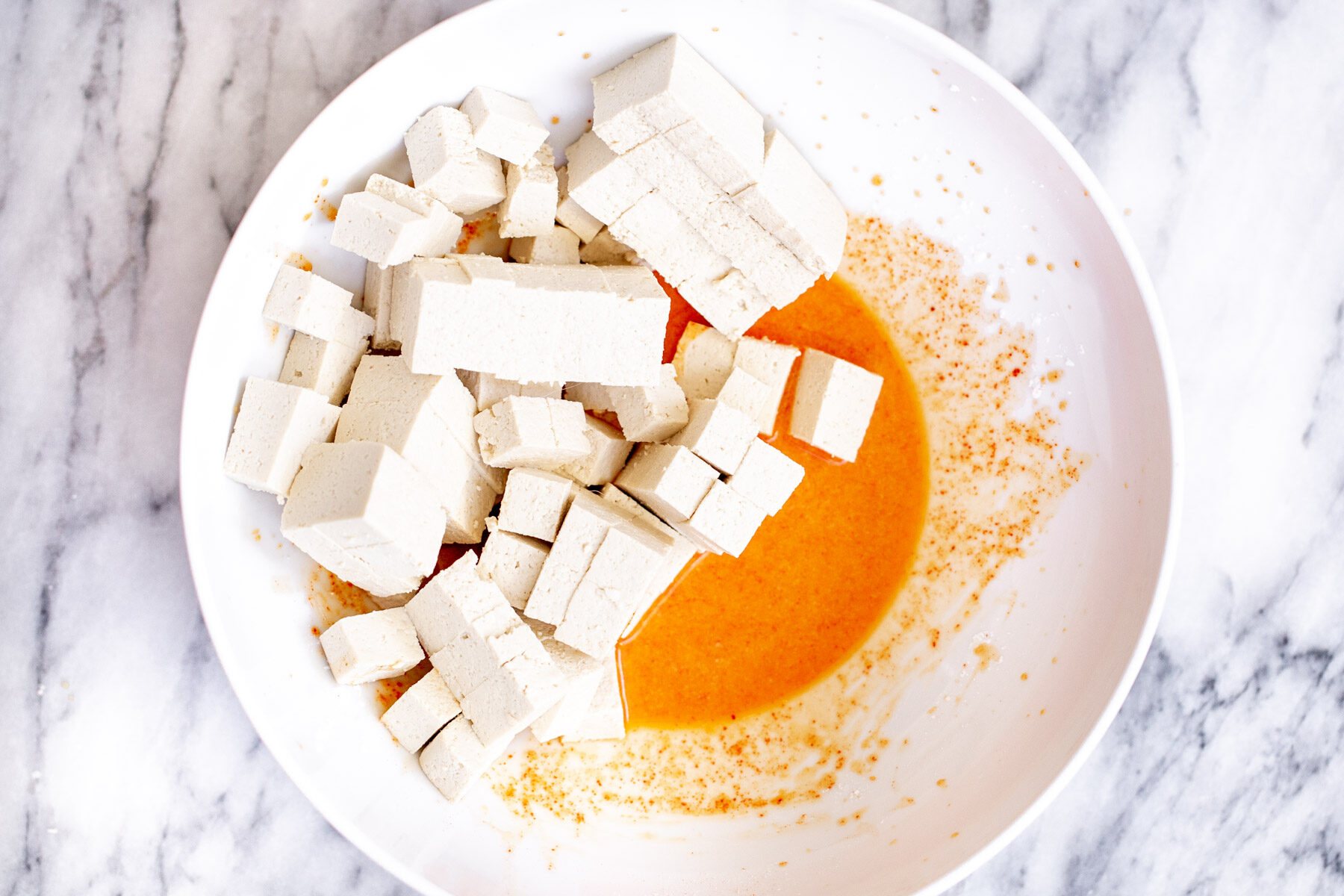 tofu cubes on a white plate mixed with spices and cornstarch