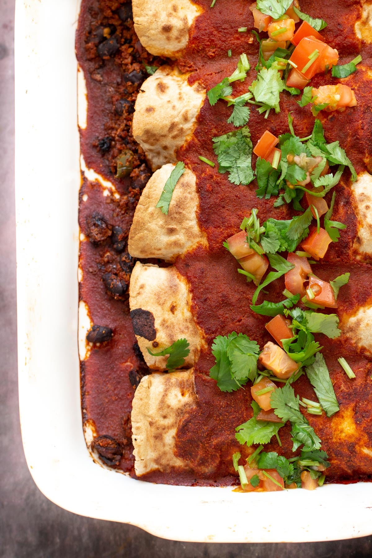 a casserole dish with vegan enchiladas covered with tomato sauce and topped with cilantro