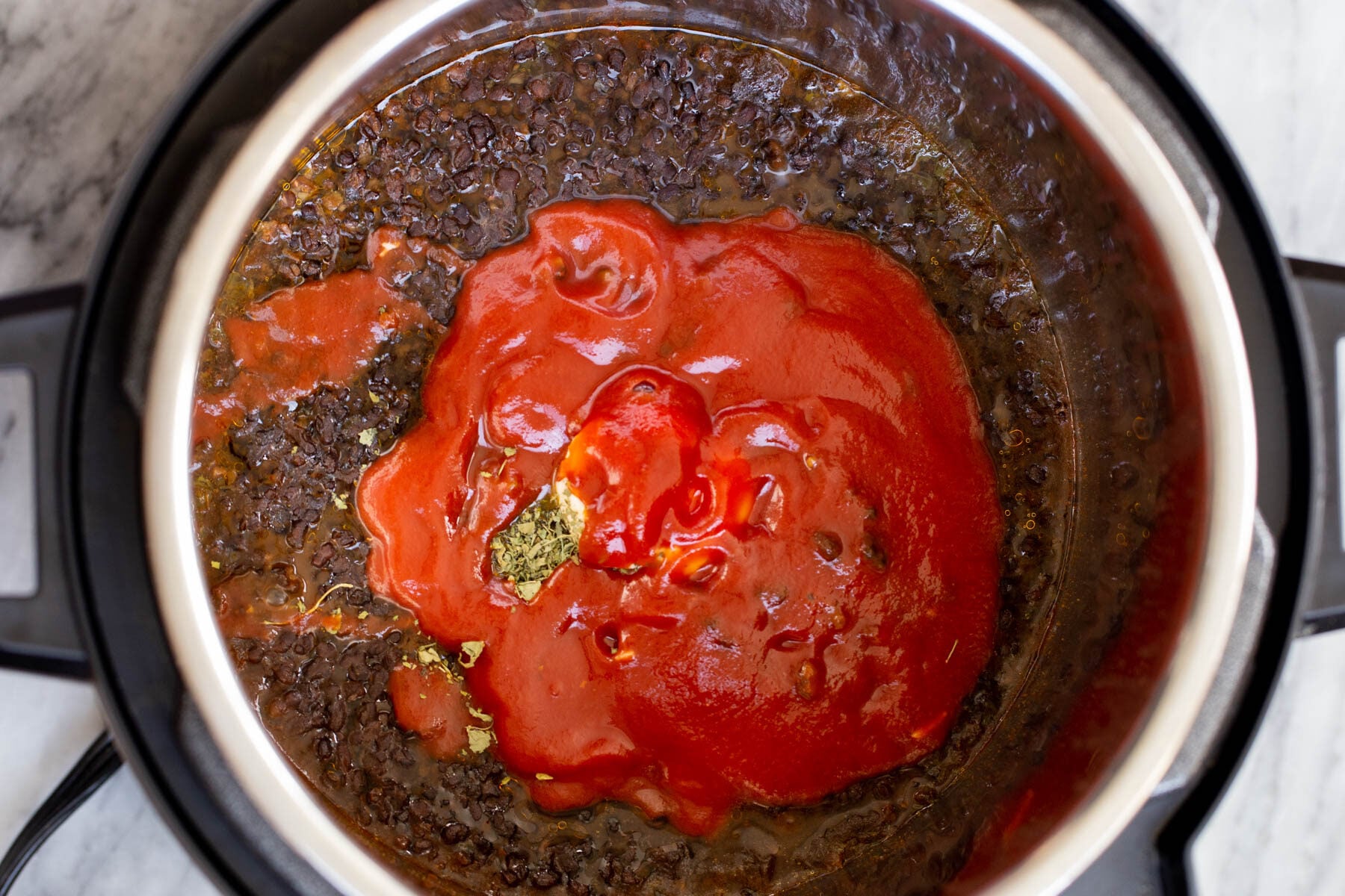 tomato puree being added to cooked black gram in an Instant Pot