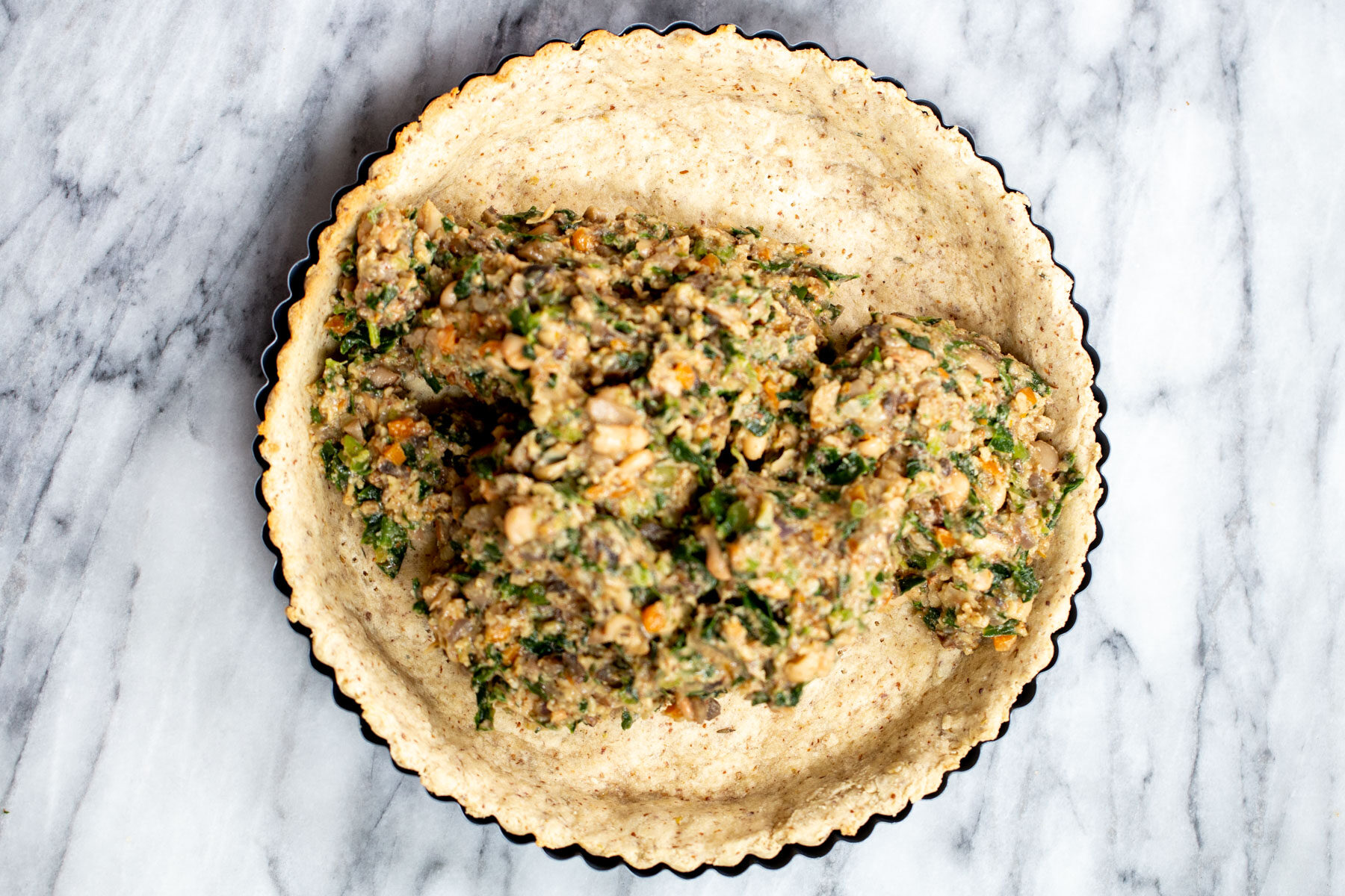 vegan spinach mushroom filling being added to savory pre-baked crust