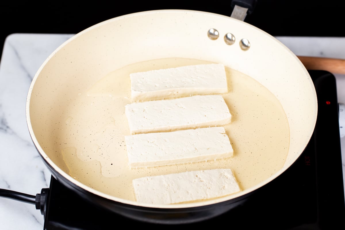tofu wedged being added to a pan with oil 