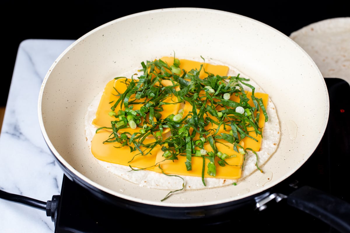 tortilla topped with vegan cheese and chopped greens in a pan 
