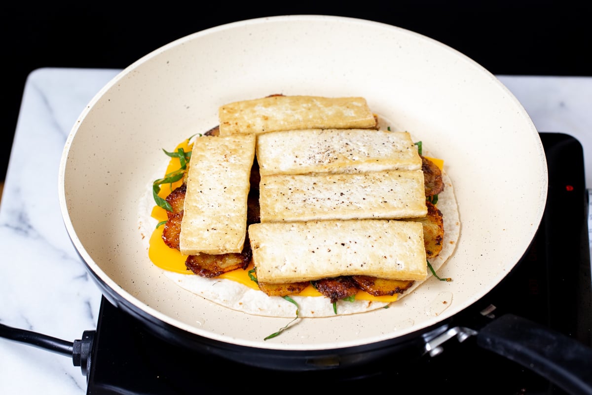 vegan quesadilla being topped with cheese and tofu slices 