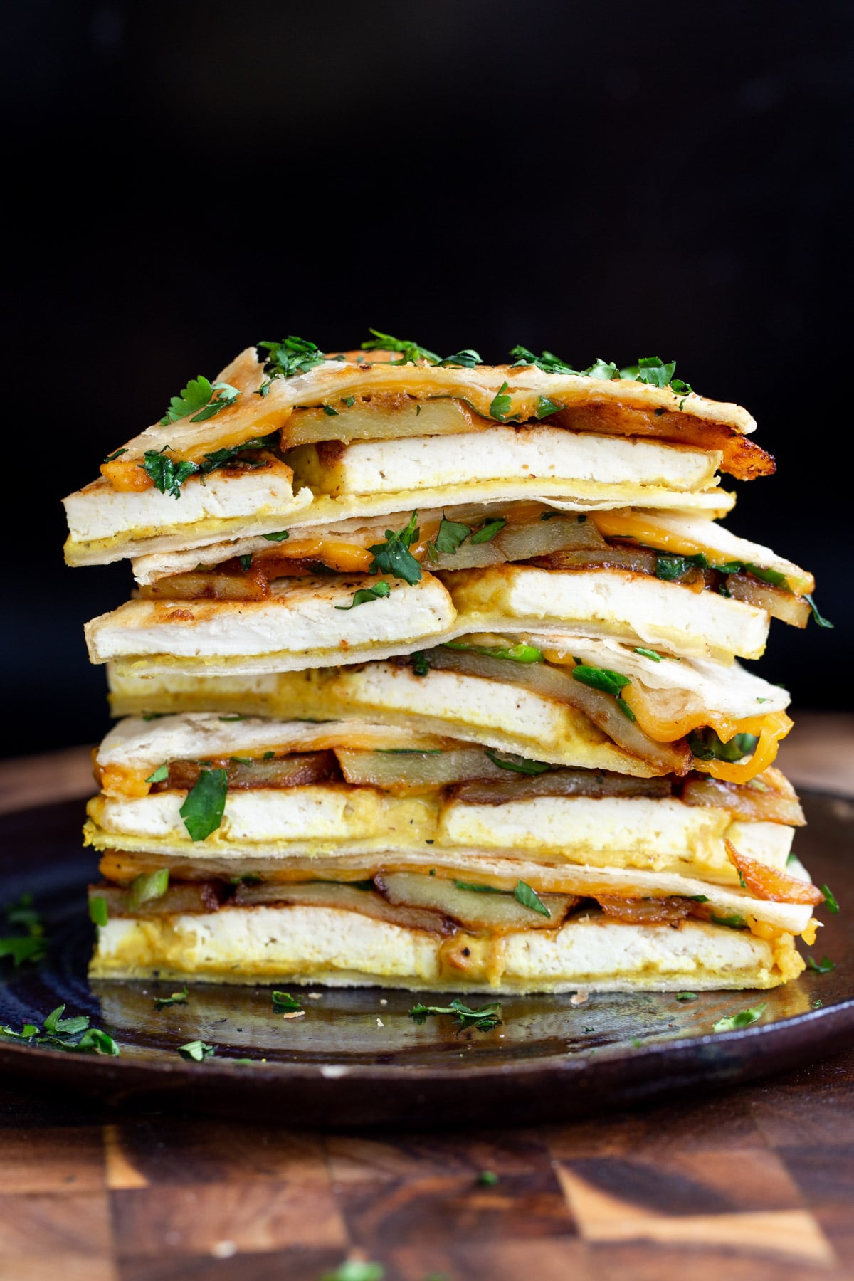 stacked wedges of vegan breakfast quesadilla with potatoes and tofu topped with cilantro 