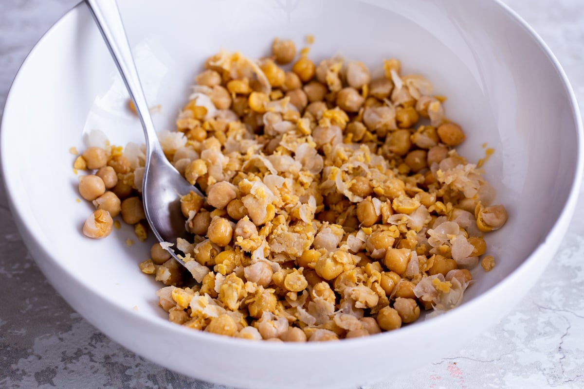 chickpeas being mashed with spices in a white bowl