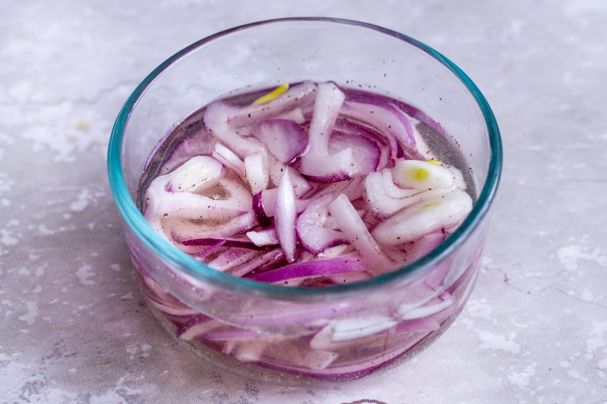 sliced red onions being added to a small bowl with brine to make pickles
