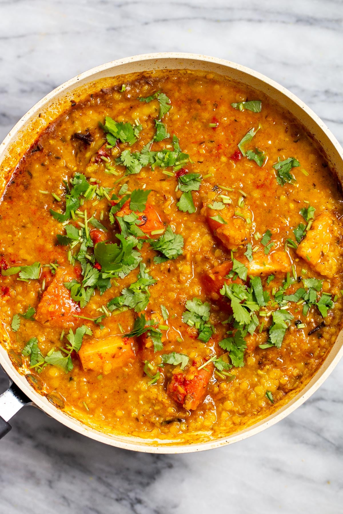 a sauteeing pan with red lentil butter dal sprinkled with cilantro