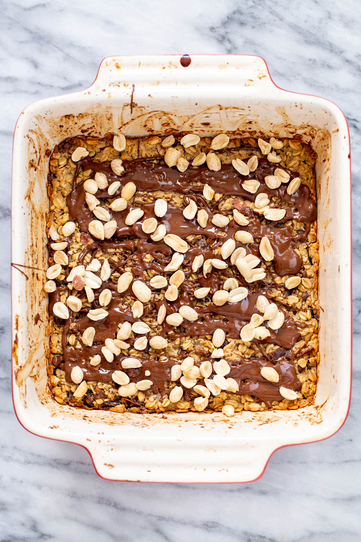 a casserole dish with peanut butter baked oatmeal topped with melted chocolate and peanuts
