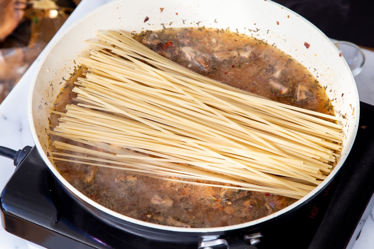 dried pasta being added to a pot with mushroom tomato sauce