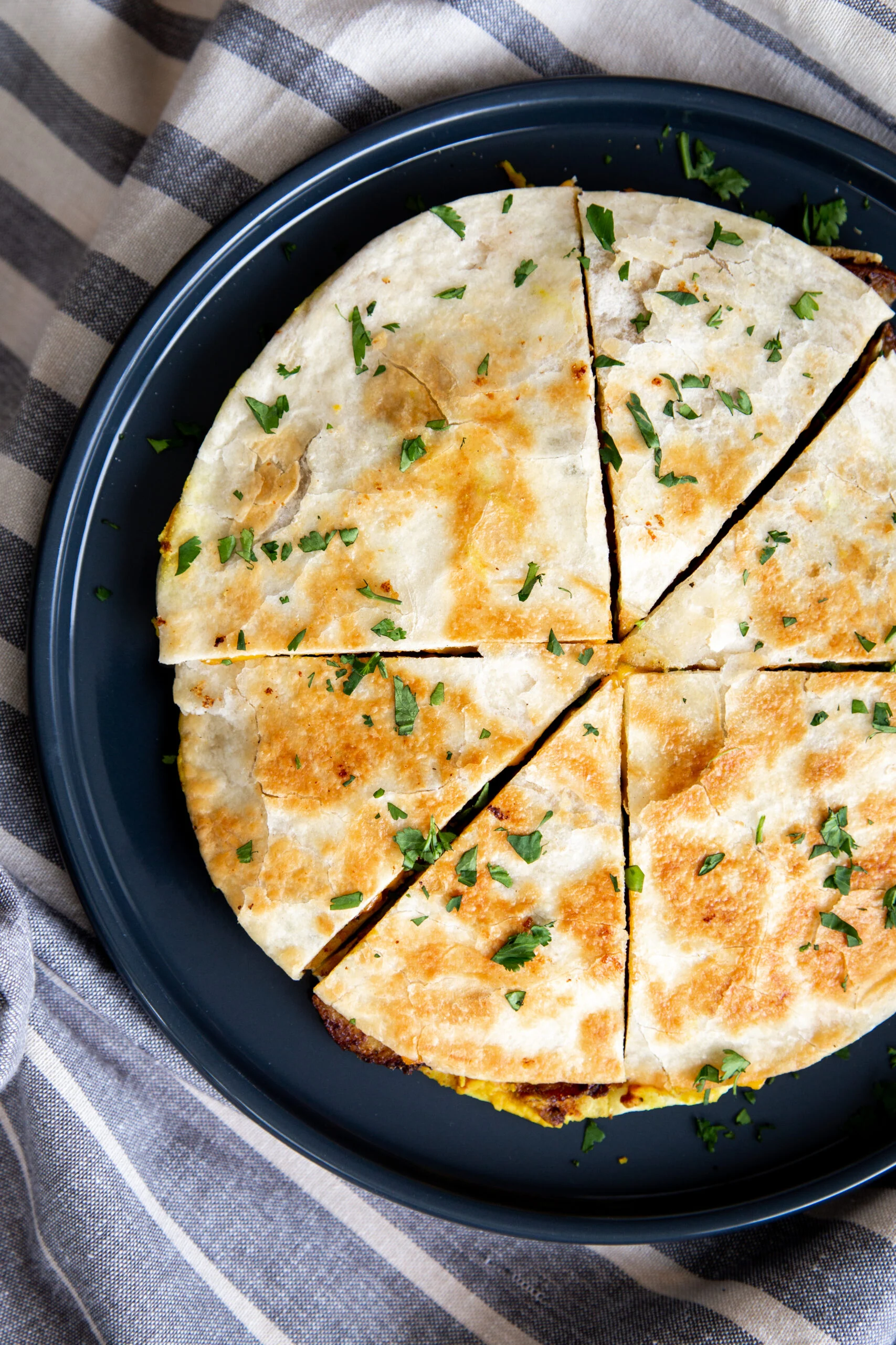 overhead shot of vegan breakfast quesadilla cut into wedges sprinkled with parsley 