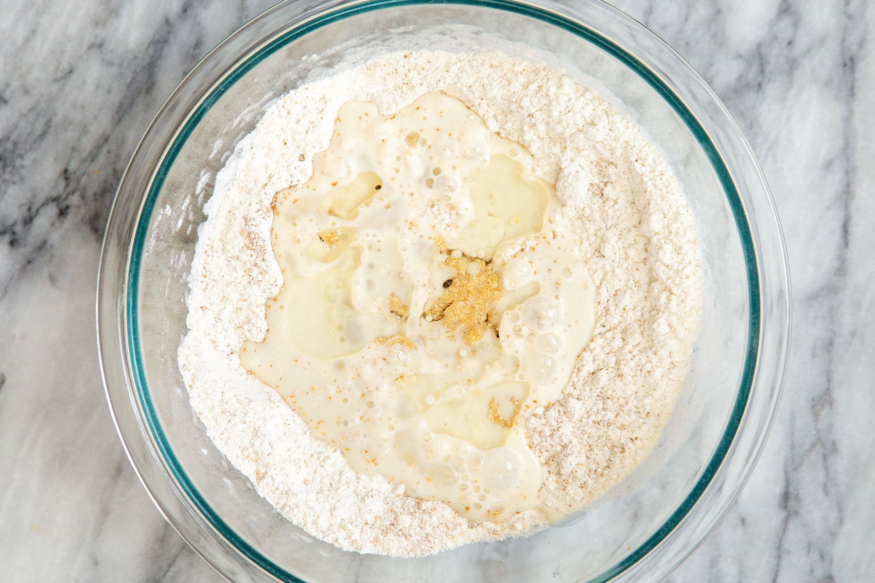 milk being added to dry ingredients in a glass bowl 